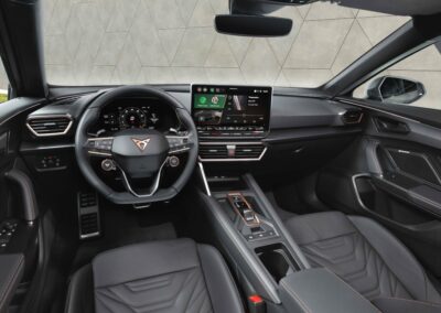 Wnętrze Cupry Formentor, zdjęcie zrobione z miejsca kierowcy, widać deskę rozdzielczą z dużym ekranem. Wszystko wykończone w czarnej barwie ze złotymi elementami.