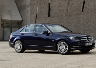 Granatowy Mercedesy klasy C W204zaparkowany przed budynkiem widoczny prawy przodo-bok