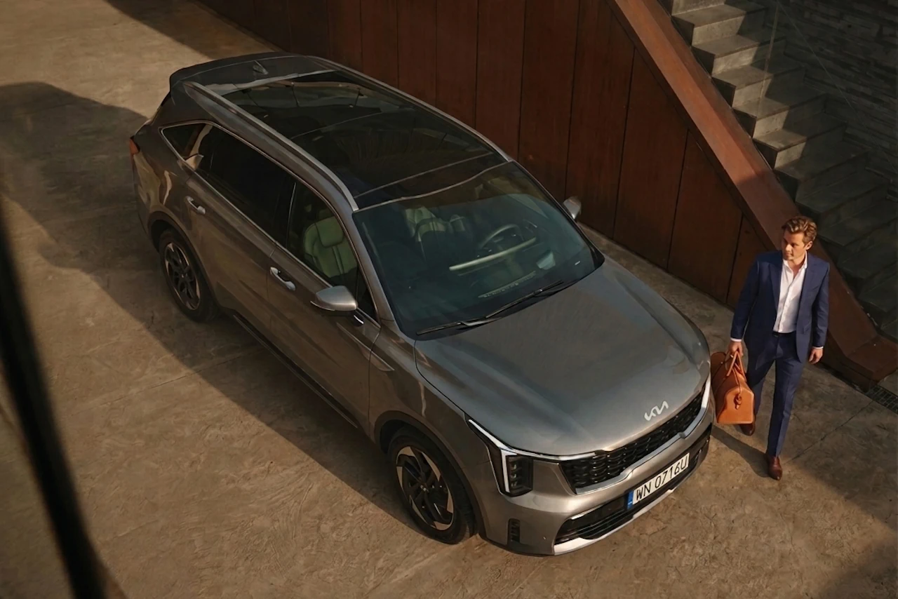 kia sorento adwert 4 Beżowa Kia Sorento stoi przed budynkiem, obok idzie mężczyzna, widać dach, przód i prawy bok samochodu