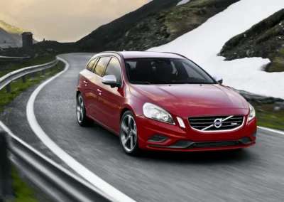Czerwone Volvo V60 1 generacji jedzie na zakręcie w górach, widać przód i prawy bok auta