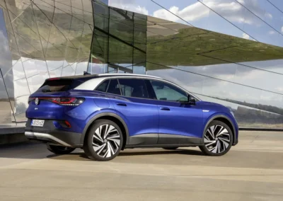 Niebieski Volkswagen ID.4 stoi przed szklanym budynkiem, widać tył i prawy bok auta