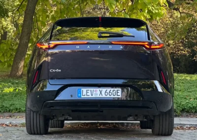 Fioletowa Mazda CX-6e stoi na brukowanej drodze – widać tył auta, w tle są drzewa.