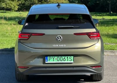 Volkswagen ID.3 Neo stoi na asfaltowej drodze – widać tył auta, w tle są drzewa.