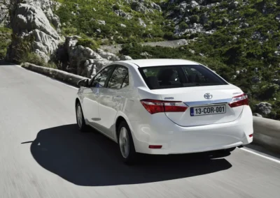 biała Toyota Corolla 11 generacji (e170) jadąca drogą wśród skał. Widok na lewy tył auta